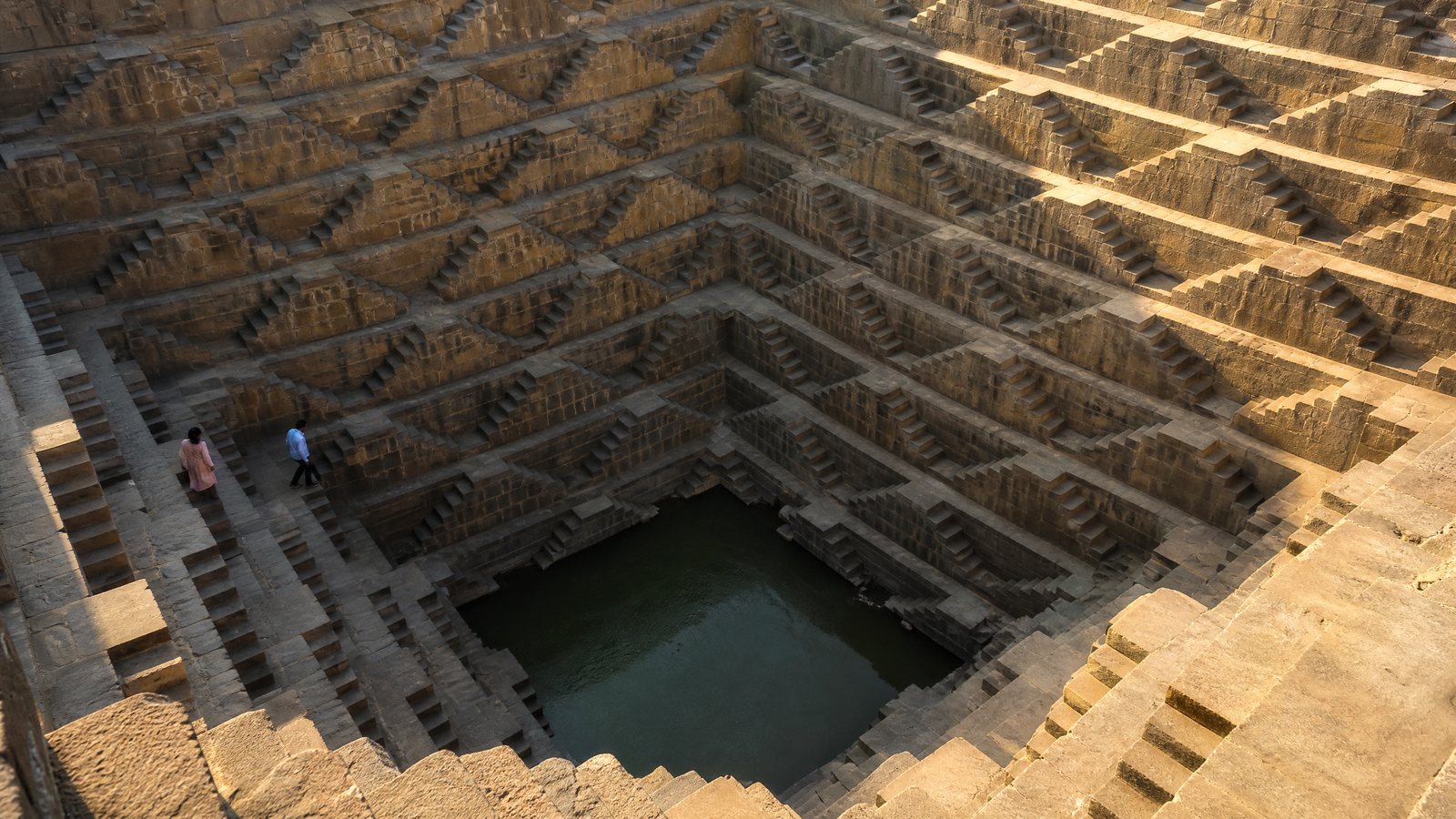 Geometric sandstone stairs descending into a Rajasthan stepwell in morning shadow